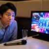 カラオケの画面に表示された80点のスコアを見て考え込む日本人男性。「DAMで80点は下手なのか？」という疑問を表すイメージ。