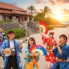 沖縄の美しい風景を背景に、華やかな琉球衣装をまとった沖縄出身の芸能人たちが歌や踊りを披露している様子。沖縄の文化と芸能界のつながりを示す。